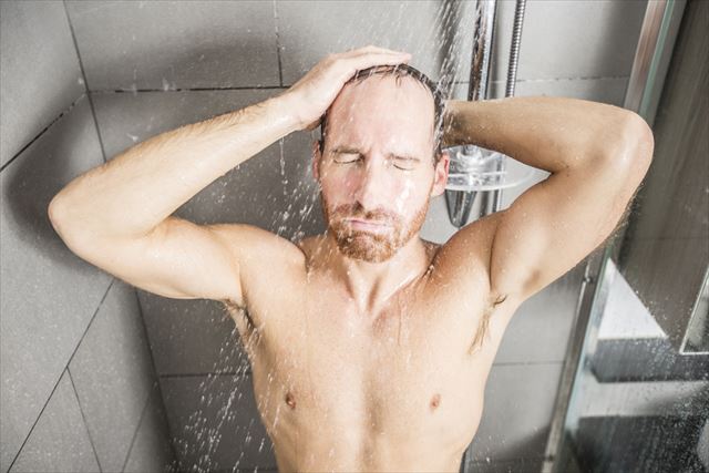 シャンプー前にお湯で予洗いする男性の画像