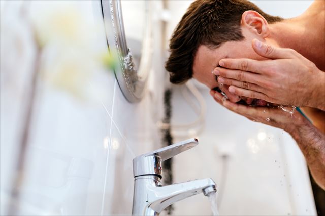 強い力でこすって顔を洗う男性の画像