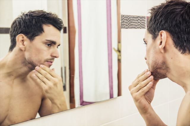 時分の肌質を鏡でチェックする男性の画像